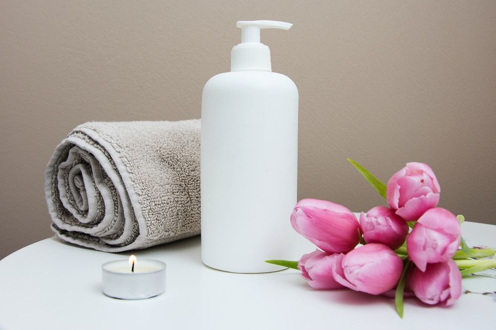 white plastic pump bottle beside pink tulips and gray towel - Exfoliants to Heal Adult Acne Skin