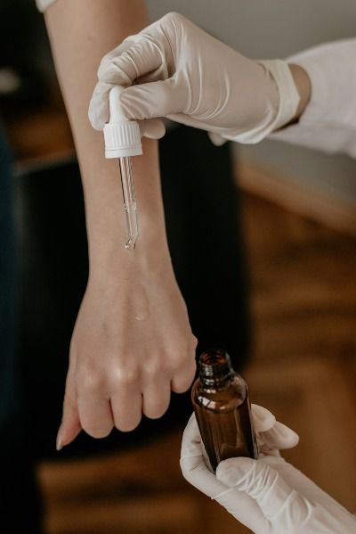 person with white gloves holding drop bottle pointing on another person's hand-  Acne Serums