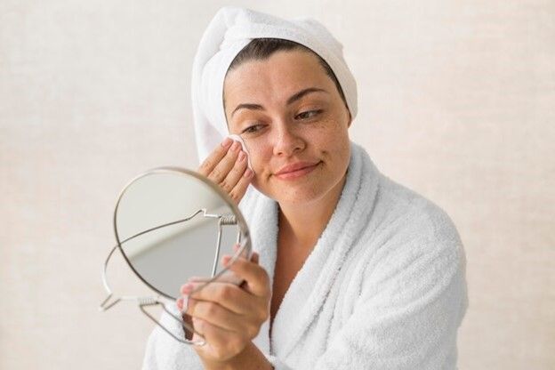 girl with white towel and toweling gown holding mirror to her face