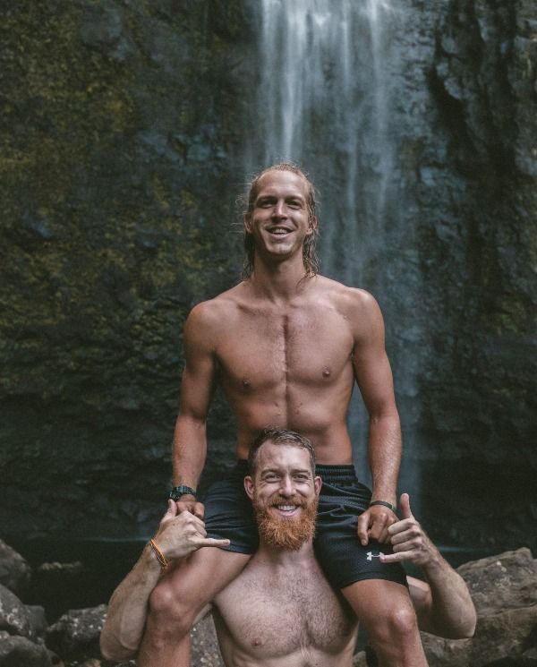 a man is holding a man on his shoulders in front of a waterfall