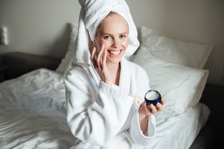   happy-smiling-woman-bathrobe-putting-cream-face - Skincare Routine for Acne