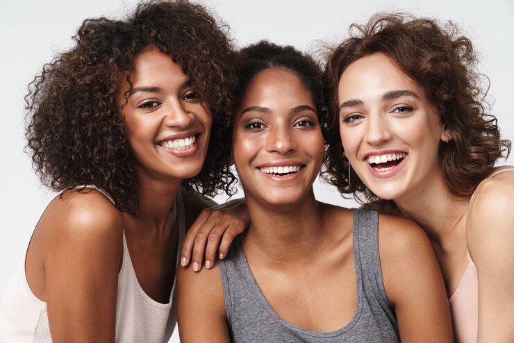 Photo portrait of three young multiracial women standing together and smiling at camera - Biotin oil for hair