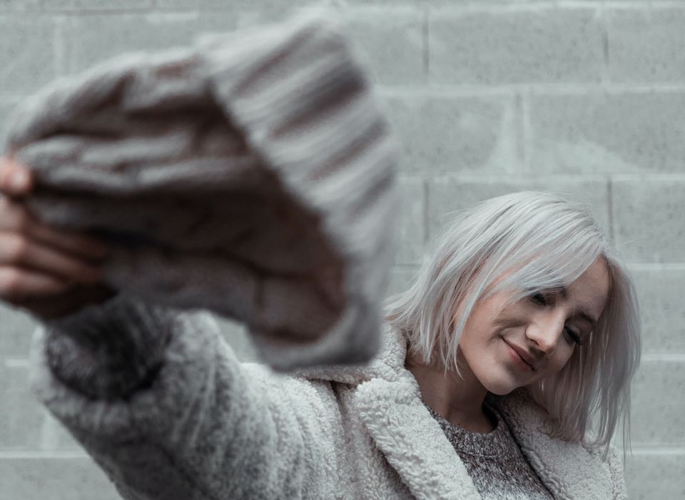 lady with grey hair flinging woolen cape on a grey brick background - Shampoos and Hair Care