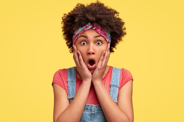 Portrait on a yellow background of young woman with curly hair with stupefied expression